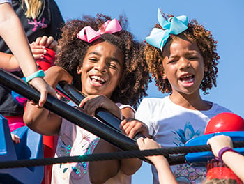 Two children smiling and laughing on top of a playground climber