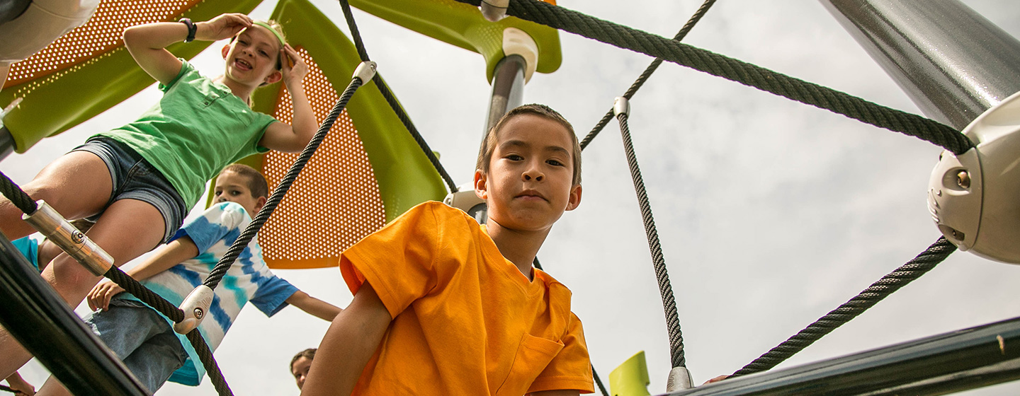 Young boy and girl looking down from a outdoor Netplex playground rope climber.