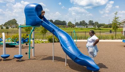 A boy prepares to slide down a standalone Rushwinder slide on a playground while a woman watches from below