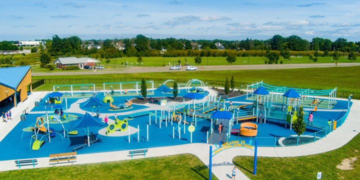 Distant aerial photo of a large brightly colored playground with swimming pool blue surfacing and neon colored playground components. 