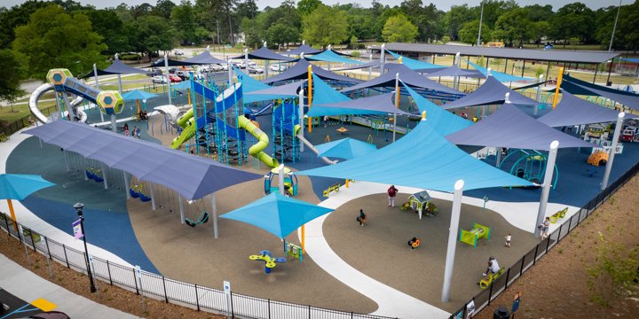An expansive playground shaped like a half-circle with many blue triangular shade sails over the top. 