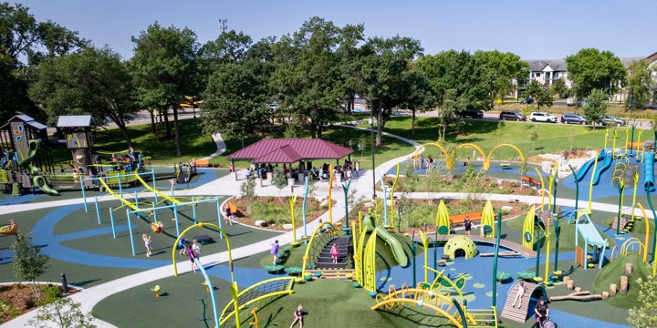A large playground with many arch-shaped playground elements and a purplish shade structure over a green and blue surfacing. 