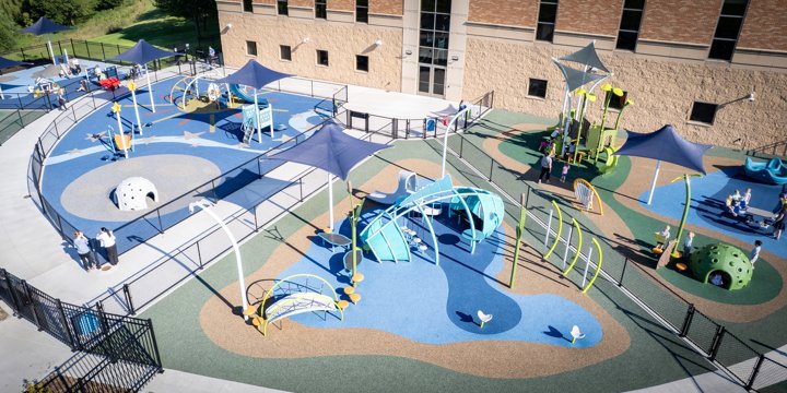 A large half-circle shaped playground cut into three wedge shaped sections, with different colored surfacing and playground structures in each section. 
