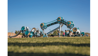 Three separate futuristic like play structures have hexagonal play pods all connected by climbers, slides, and belted pathways. One structure is three towers with a single hexagonal pod on the top, enclosed crawl tunnels connect the play pods.